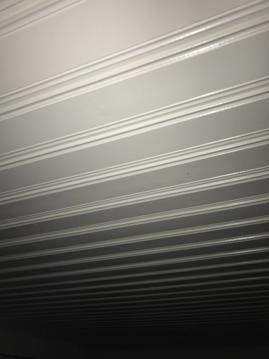 Vitmålad Morapanel med flera lager färg, synliga skarvar och struktur i stugtak.