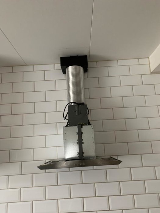 Köksfläkt utan synbart ventilationshål monterad mot en vit kaklad vägg under ett sluttande vitt tak.