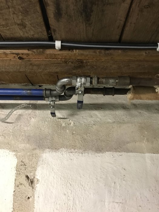 Avluftningsventiler monterade på vattenrör under träbjälkar i ett källarrum.