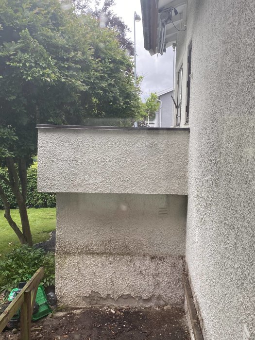 Yläterassi ja seinä 1940-luvun funkistyylisessä talossa, seinärakenteet näkyvät. Taustalla puutarha ja kasvillisuutta.