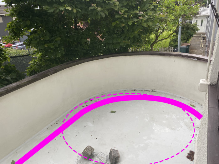 Pyöreä terassi, jossa betonilattia ja seinästö, ympäröivä vehreys. Lattialla muutama kivi ja vaaleanpunainen viiva merkitsemässä mahdollisen kylpylän paikkaa.