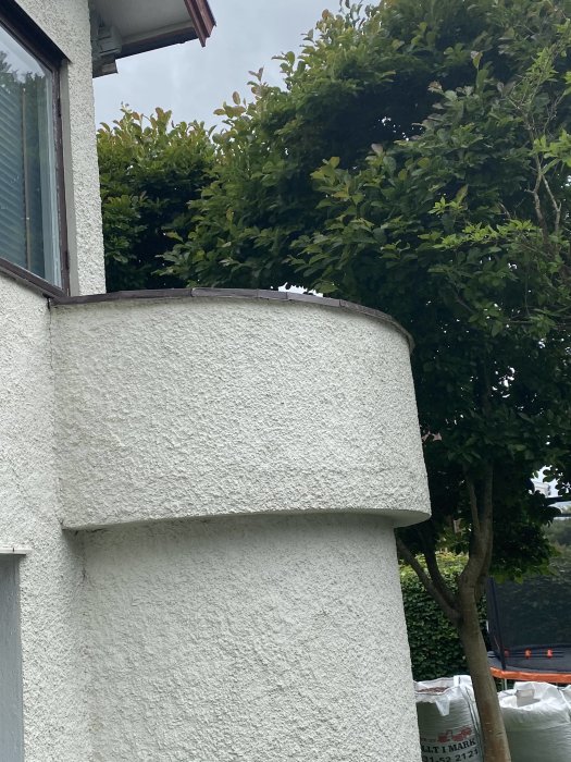 Pyöreä valkoinen parveke 1940-luvun talossa, ympäröitynä vihreillä puilla. Olisiko kestävä ulkoporealtaalle?