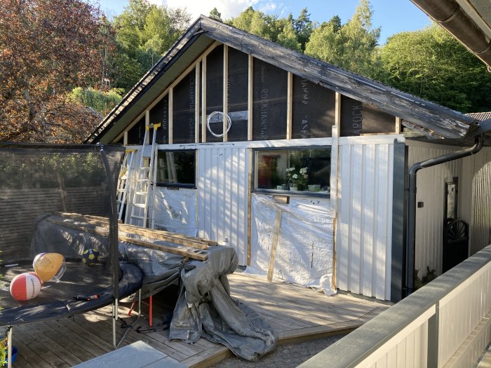 Hus under renovering med nyuppsatt stående vit panel och väntande byggmaterial.