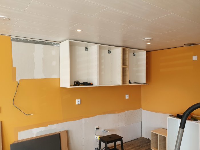 Kök under renovering med ommålade väggar och delvis monterade IKEA-överskåp, bänkskåp och elinstallationer synliga.