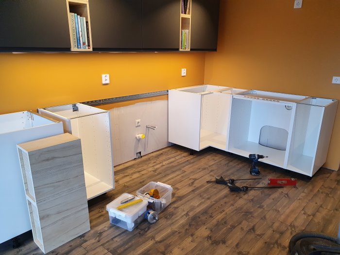 Pågående installation av IKEA köksskåp med överskåp monterade och bänkskåp under uppbyggnad, verktyg på golvet.