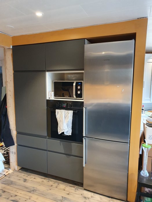 Modernt, grått IKEA kök med inbyggda vitvaror, inklusive mikrovågsugn, ugn och stor kyl/frys, samt trädetaljer.