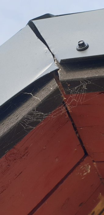 Detaljbild på skadad vindskiva med sprickor och spindelnät på husets gavel.