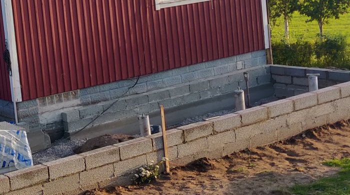 Grundkonstruktion av sten med vattenavrinningrör vid sidan av en byggnad under konstruktion.