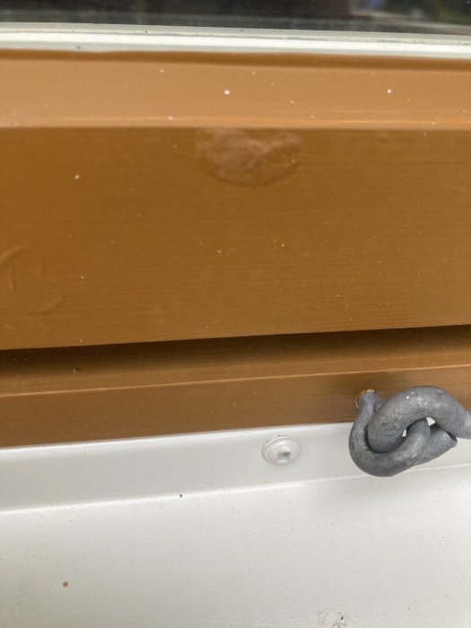 Nymålat träfönster med en bubbla i linoljefärgen på den bruna karmen nära ett fönsterspärr.
