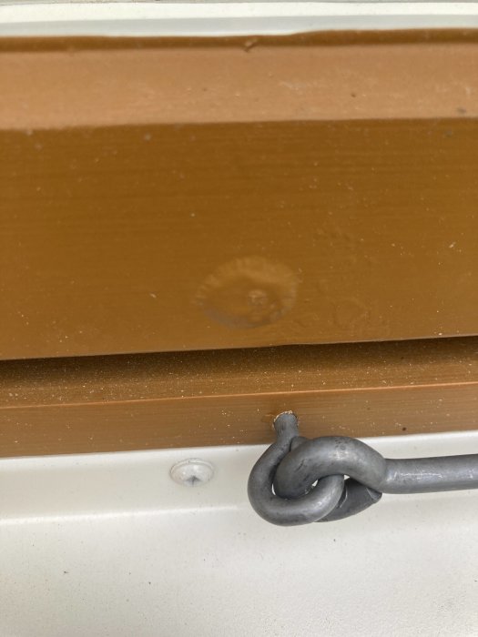 Nymålat träfönster i brun linoljefärg med bubblor i färgskiktet nära fönsterhaspen.