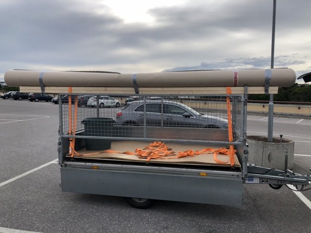 Släpvagn lastad med byggmaterial, säkrat med band och tejp, på en parkeringsplats.