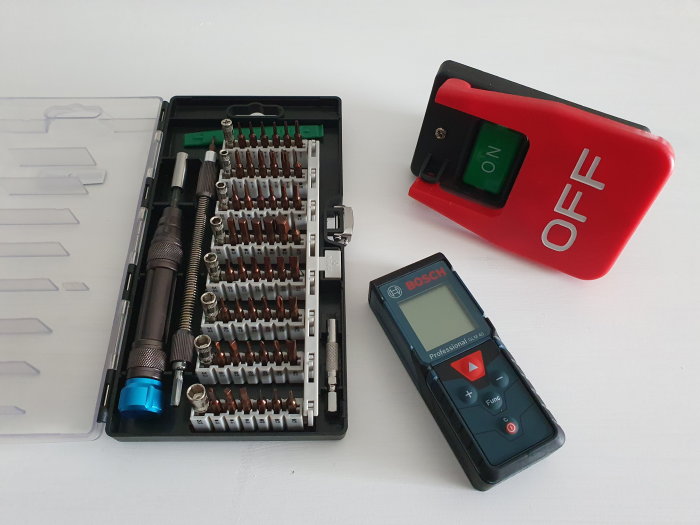 Ett öppet bitssatsfodral vid sidan av en röd och grön strömbrytare och en Bosch laseravståndsmätare.