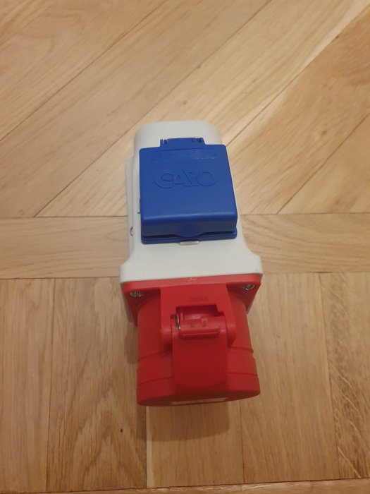 En CEE 3N/16A+Shuko-uttag mot trägolv med märkning GARO på det blå locket och röd botten.