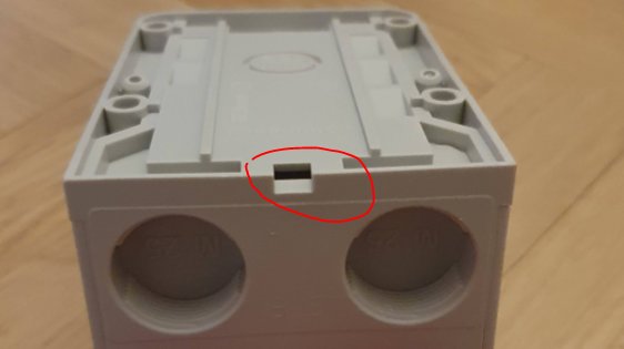 Grå plastdosa med framexponerat Schukouttag och öppet dräneringshål markerat med röd cirkel.