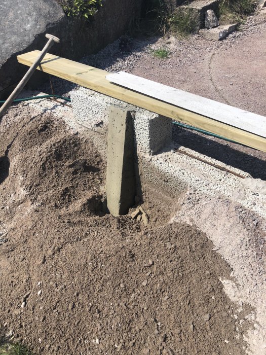 En nyligen gjuten betongkontrefor, ca 10 cm bred och 20 cm djup, förankrad i muren, med omgivande grus och verktyg.