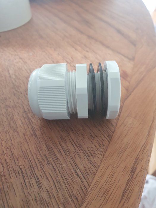 En vit plastgenomföring M25 på ett träbord, avsedd för elektriska installationer.