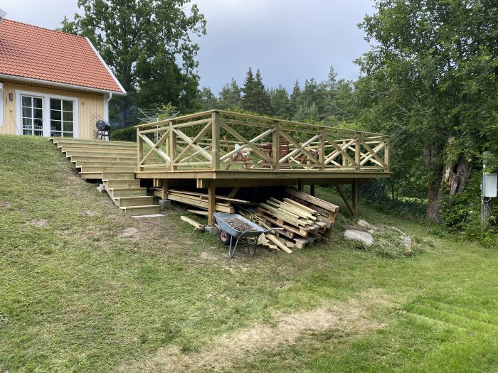 Nybyggd oavslutad trädäck med räcke bredvid ett hus, material och verktyg syns under.