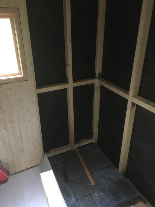 Pågående renovering av en bastu med nytt golv av sibirisk lärk, väggar med påbörjad bastupanel och reglar för framtida installation av bastulav och skydd.