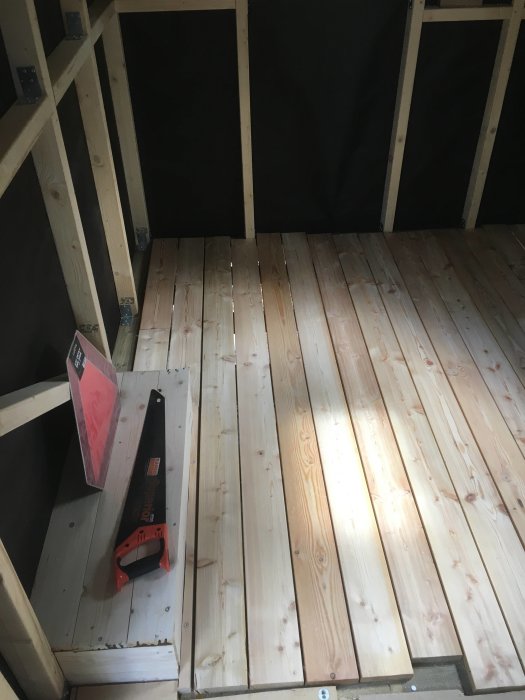 Ny lagt golv av sibirisk lärk i ett pågående bastubygge med verktyg och reglar synliga.