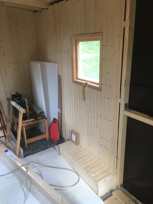 Nybyggt basturum under konstruktion med lärkgolv, omonterade bastupaneler och stenplatta under framtida ugn.