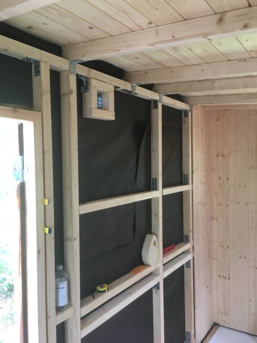 Halvfärdig bastuinteriör med träreglar och isolering samt påbörjad bastupanel på väggar.