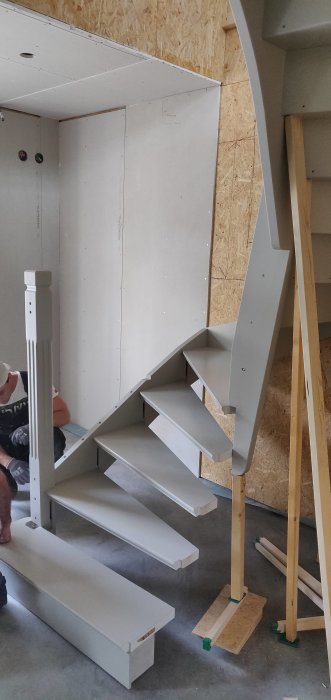 Nyinstallerad vit trappa i ett hus under renovering, med osynliga väggfästen och trästöd.