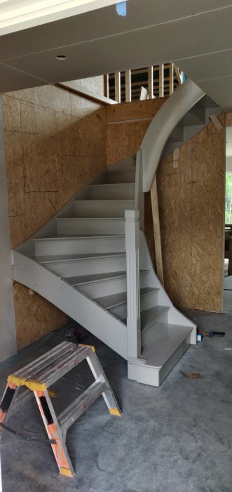 Nyinstallerad grå spiraltrappa i en byggarbetsmiljö med OSB-skivor och en stege.