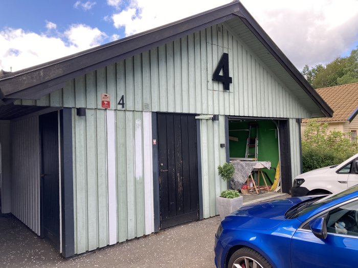 Garage med öppen dörr och synliga renoveringsverktyg, delvis rivna väggar, och en stege inuti.