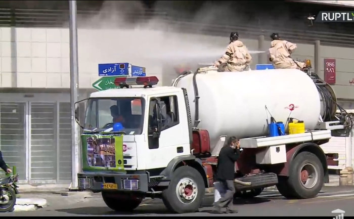 Desinficeringsåtgärder i Iran med personer som sprutar vätska från tankbil på en stads gata under pandemin.