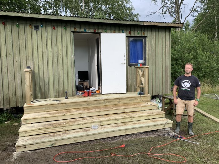 Man står framför nyligen byggd trätrappa till husvagn med verktyg och byggmaterial utspridda runtomkring.