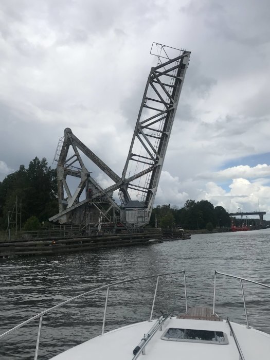 Vy från båt mot öppen vikbar bro under molnig himmel.