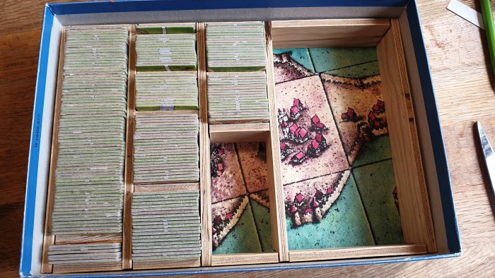 Träinsats för Carcassonne-brädspel med ordnade fack fulla av spelbrickor och anpassad för expansioner.