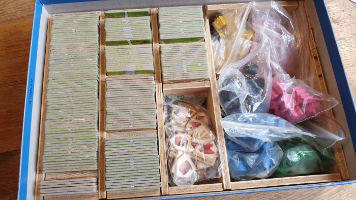 Organiserad lådinsats för Carcassonne-spel med sorterade spelkort och färgade pjäser i plastpåsar.