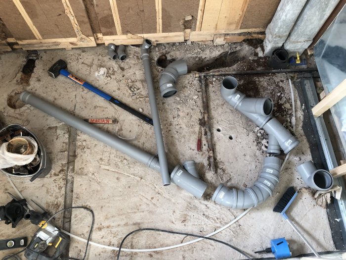 Installation av gråa PVC-avloppsrör på ett bygge med kurvor och kopplingar, delar av åtkomstgolv synligt.