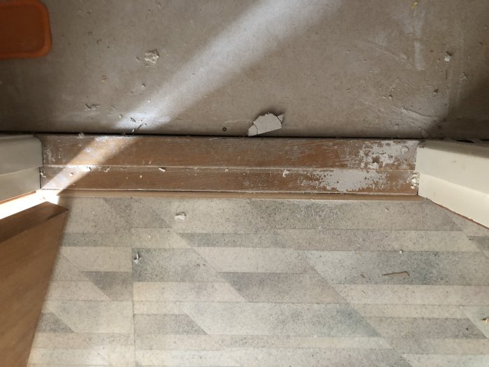 Nedsliten badrumströskel vid dörröppning som behöver höjas, med golv i förgrunden.