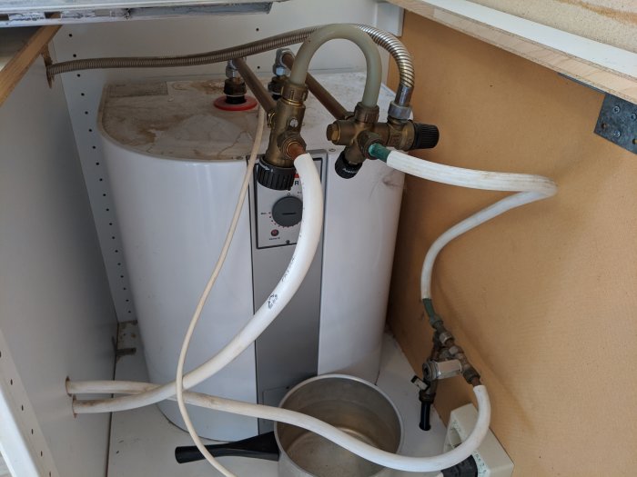 Rörinstallation med varmvattenberedare, kallvatteninlopp, blandareanslutning och dräneringsslang i skåp.