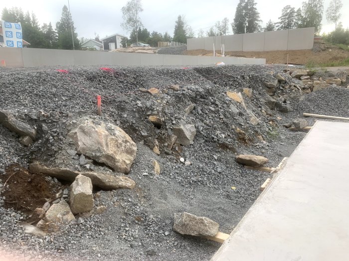 Slänt med sprängsten och makadam bredvid en poolplatta, markerat för planerad trappa.