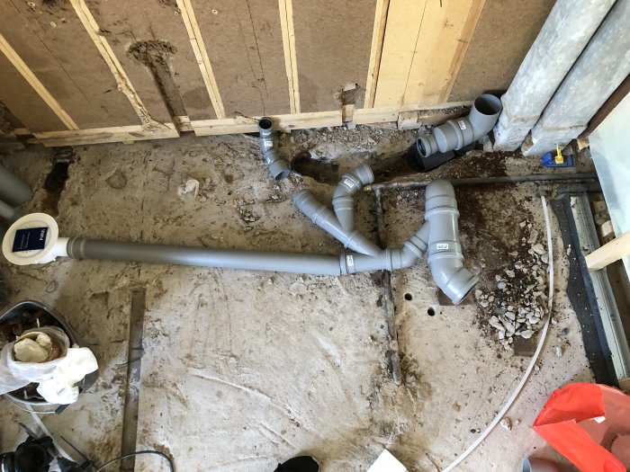 Nyinstallerade avloppsrör med få böjar i en byggarbetsplats passerar under befintlig vattenledning.
