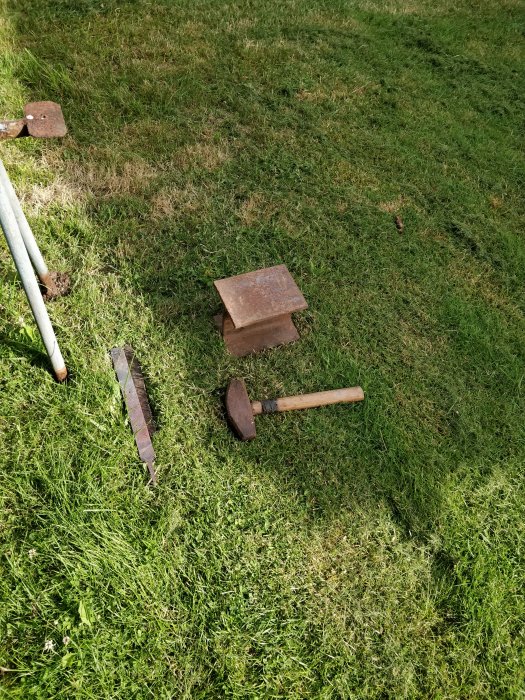 En hobby-ässja och hammare på en gräsmatta, antyder smidesarbete utomhus.