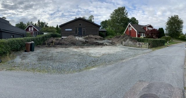 En upprivet tomt med högar av grus och jord bredvid en asfalterad gata i ett bostadsområde.