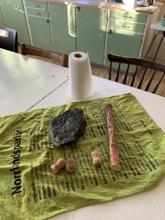Material till pappersrullehållare på duk: köksrulle, skiffersten, björkgren och champagnekorkar.
