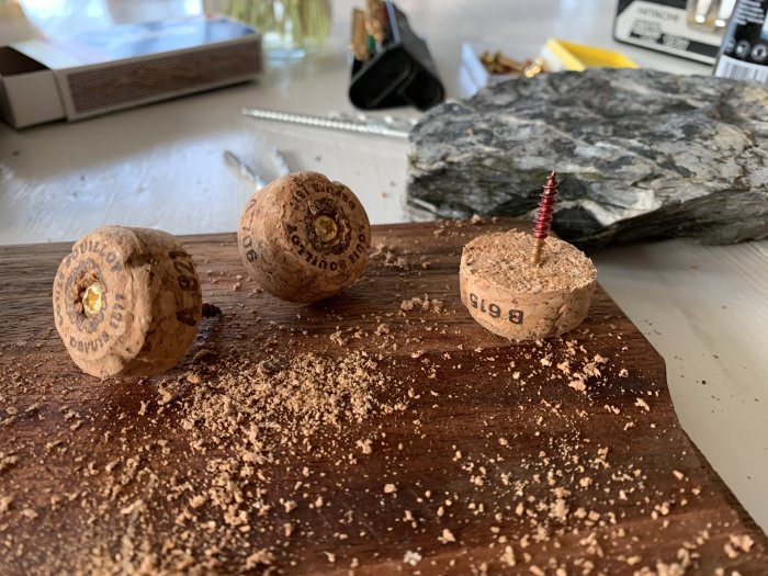 Champagnekorkar med inskruvade skruvar på ett bord med sågspån, bakgrunden visar en skiffersten.
