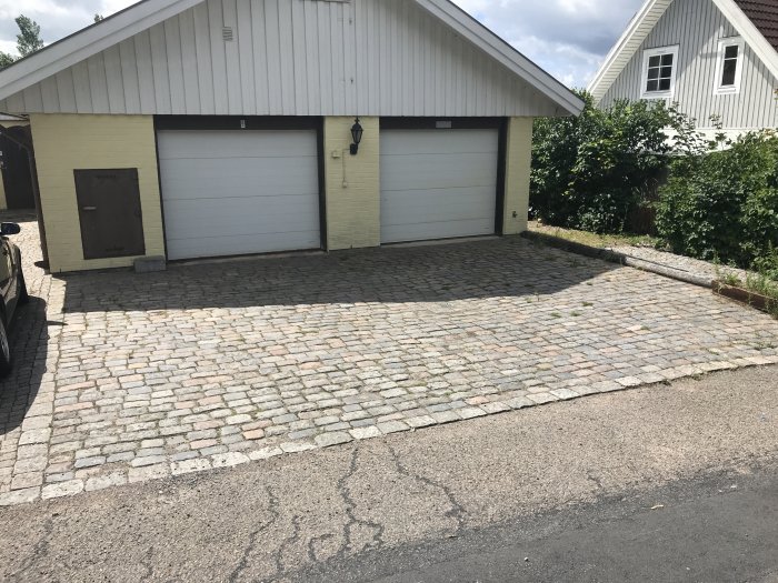 Uppfart av gatsten framför vit garagebyggnad, olämplig för skateboard och basket.