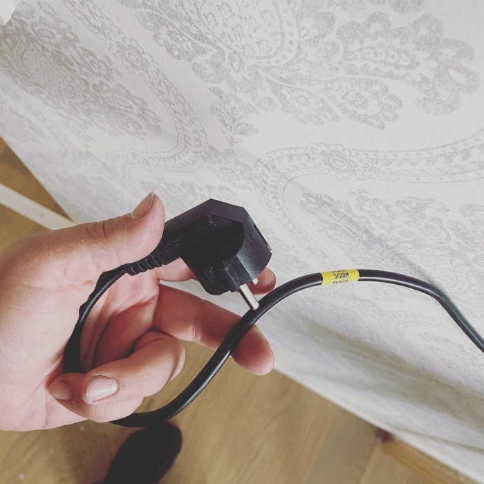 Hand håller en elkontakt med en skadad kabel som visar blottade trådar.