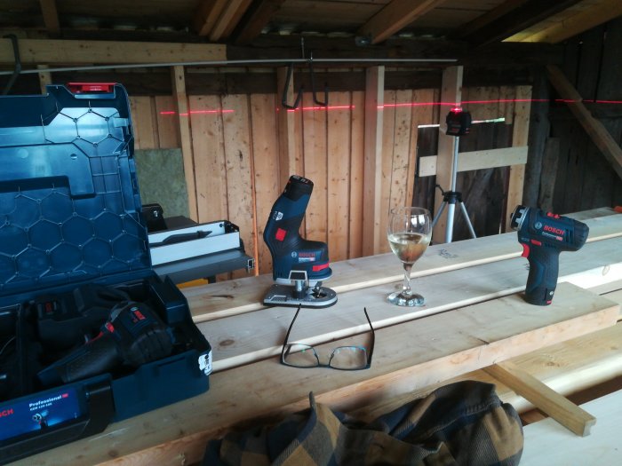 Verktygsuppsättning med Bosch borr, laserinstrument och ett glas på ett träbord i halvfärdigt byggprojekt.