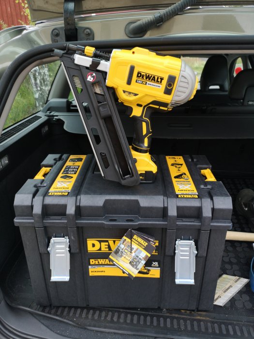 Ny Dewalt spikpistol på en robust verktygslåda i en bilens bagageutrymme, redo för panelbyte.