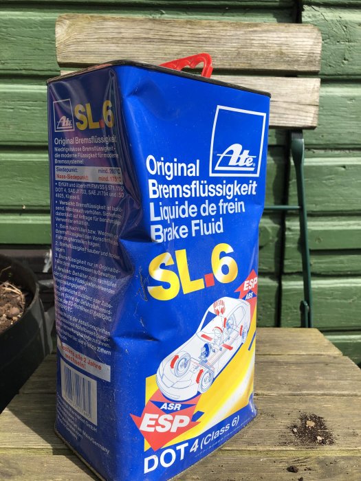 Beskadigad förpackning av ATE SL6 bromsvätska, utvidgad på botten och ihoptryckt upptill, står på ett träbord.