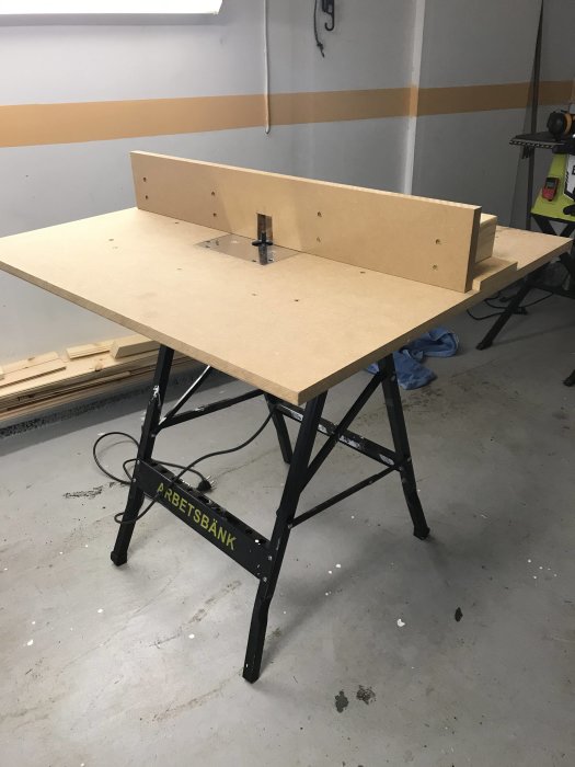 Egetbyggt fräsbord i garagemiljö på svart arbetsbänk, med oskyddad fräs monterad.