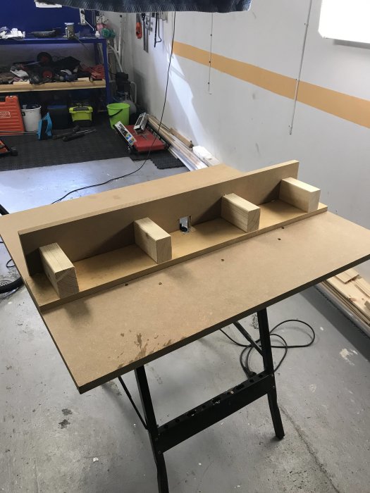 Hembyggt fräsbord av trämaterial på ett metallställ i ett verkstadsutrymme.