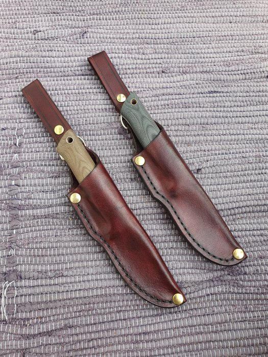 Två handgjorda läderslidor för knivar på ett grått tygunderlag.